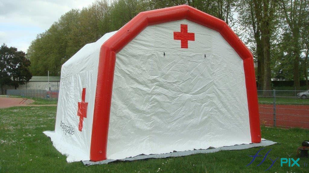 Tente PMA gonflable, face avant, avec l'entrée via une large porte pignon, et un marquage imprimé du logo de la croix rouge au dessus.