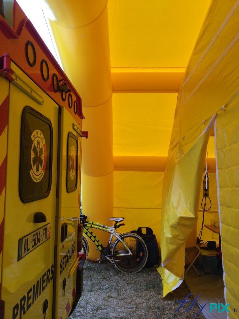 Accès à la porte de la tente PMA via une marquise adaptée. Un véhicule de premier secours est disposé sous la marquise devant le porte afin de transférer un malade ou un accidenté. Accès à la porte de la tente PMA via une marquise adaptée. Un véhicule de premier secours est disposé sous la marquise devant le porte afin de transférer un malade ou un accidenté.