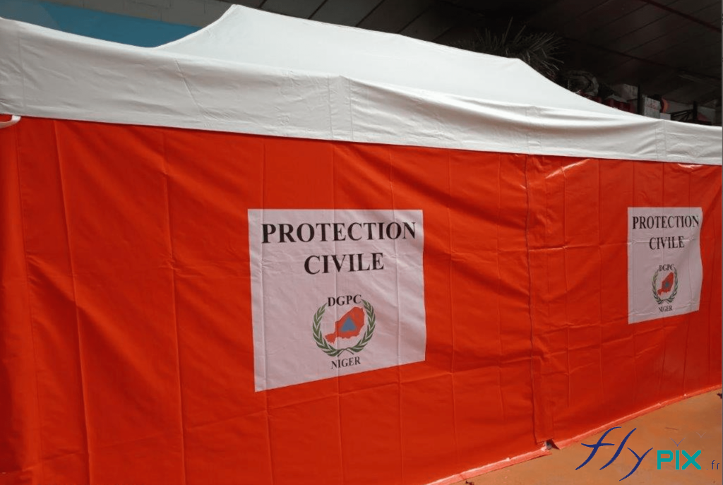 Mur de tente PMA pliable avec des marquages personnalisés en impression numérique couleur. Parmi le lot des 20 tentes médicales pliables, il y en avait 10 sur fond orange, et 10 sur fond bleu nuit. Les marquages personnalisés du logo de la Protection Civile du Niger ont été imprimés en impression numérique couleur, pour un excellent rendu visuel. Enveloppe des murs réalisés en tissu enduit biface de 450 g/m² coloris blanc – classé norme anti-feu LNE France type M2 et assemblés par coutures galonnées.