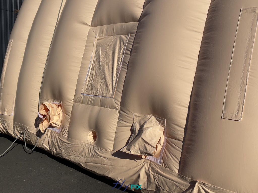 Une vue de la base d'un module gonflable, une photo prise depuis l'extérieur de la structure gonflable, qui montre différentes interfaces : une fenêtre avec un volet amovible et pliable, 2 manchons à air, et 1 trou passe fils et gaines électriques. - Copyright : Vivien LAÏLLE/FLYPIX, droits réservés. Une vue de la base d'un module gonflable, une photo prise depuis l'extérieur de la structure gonflable, qui montre différentes interfaces : une fenêtre avec un volet amovible et pliable, 2 manchons à air, et 1 trou passe fils et gaines électriques. - Copyright : Vivien LAÏLLE/FLYPIX, droits réservés.